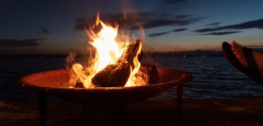 Imagem de fogueira na praia com pés em sandália ao pôr do sol, para artigo sobre o elemento fogo