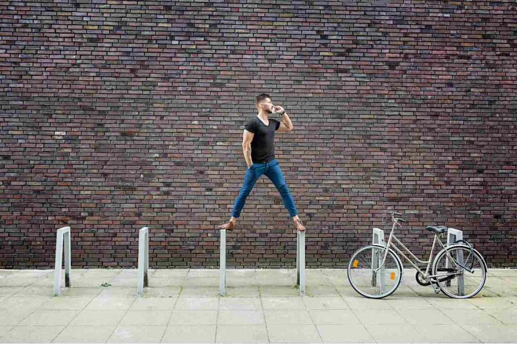 Fotografia de um homem com celular se equilibrando no bicicletário em frente a uma parede de tijolos, ilustrando a notícia sobre Mercúrio em Libra