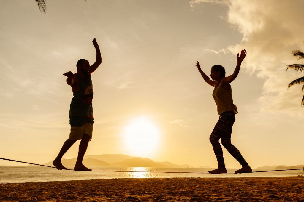 casal adolescente se equilibrando no slackline na silhueta do nascer do sol na praia, para ilustrar notícia sobre o Sol em Libra 2023