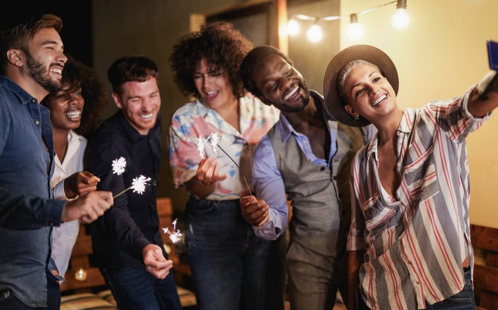 Jovens comemorando a festa de ano novo em casa ao ar livre no pátio com estrelinhas de fogos de artifício, para notícia sobre cores para o Ano Novo