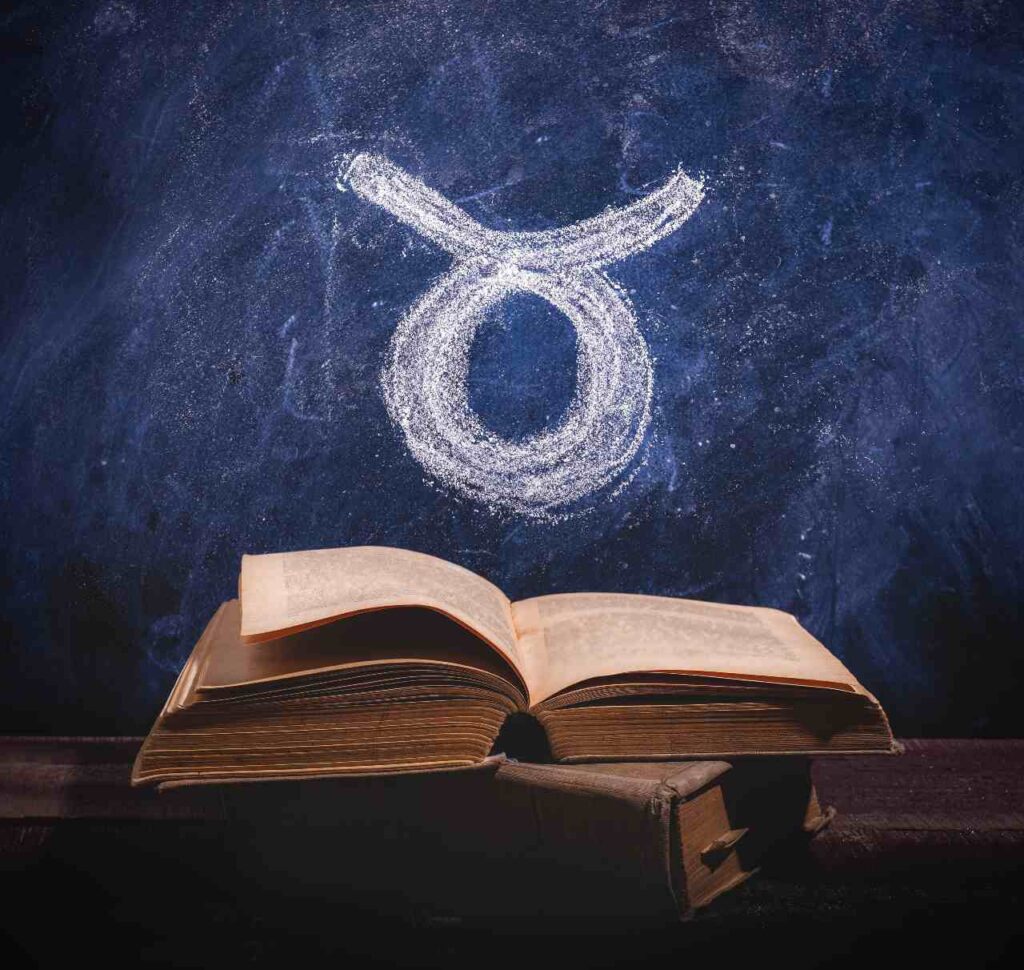 Símbolo do signo de Touro desenhado em giz em um quadro negro e um livro antigo aberto para ilustrar artigo sobre o mito de touro
