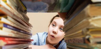 menina com interesse e curiosidade examina pilhas de livros, imagem para ilustrar artigo com dicas para o sol em Gêmeos