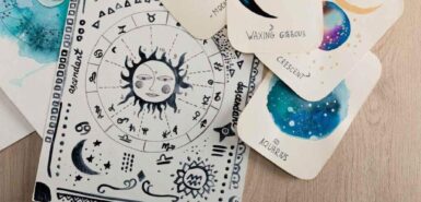Vista superior de um mapa astral ilustrado em aquarela e, ao redor, cartões com ilustrações de fases da lua e de constelações em uma mesa de madeira, para ilustrar o horóscopo de junho para cada signo