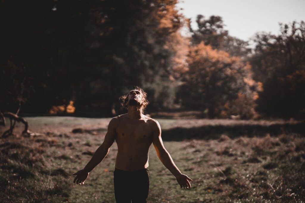 Homem espanhol de braços abertos sem camisa olhando para cima em uma floresta, para artigo que responde a pergunta se o ascendente fica mais forte depois dos 30
