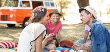 Amigos olhando para mulher rindo enquanto estão sentados no campo, para ilustrar artigo sobre a temporada de gêmeos de 2024
