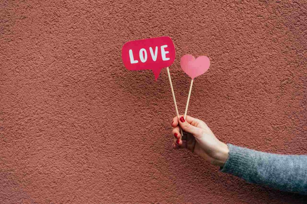 mão de uma mulher segurando pequenas placas artesanais de coração e amor, ilustrando artigo sobre como é cada signo no amor