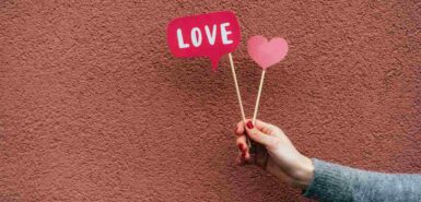 mão de uma mulher segurando pequenas placas artesanais de coração e amor, ilustrando artigo sobre como é cada signo no amor