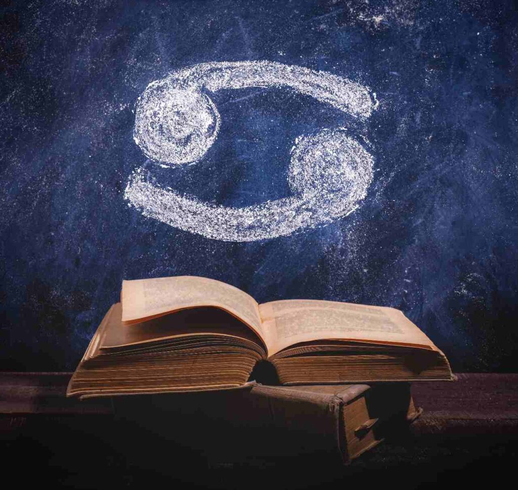 Signo do zodíaco Câncer desenhado a giz em um quadro-negro acima de livro antigo, para ilustrar artigo sobre o mito do signo de Câncer