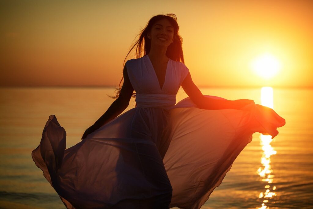 Jovem mulher livre correndo de vestido branco perto do mar ao pôr do sol