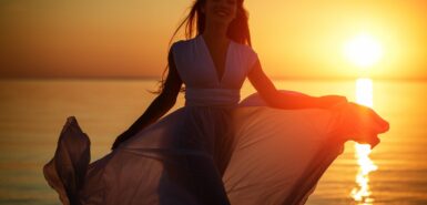 Jovem mulher livre correndo de vestido branco perto do mar ao pôr do sol