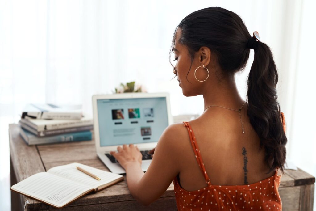 mulher verificando anotações em um caderno enquanto digita em um notebook