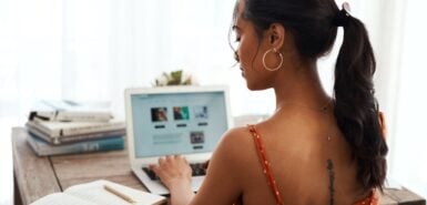 mulher verificando anotações em um caderno enquanto digita em um notebook