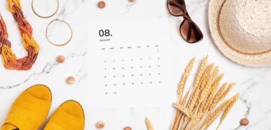 calendário de agosto sobre uma mesa de mármore, com outros objetos como colar, trigo, óculos escuros e chapéu, ilustrando horóscopo de agosto