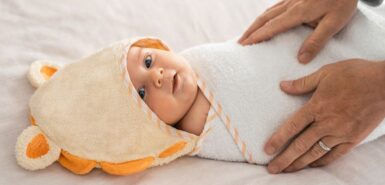 Bebê deitado e envolvido por uma toalha, mãos do pai.