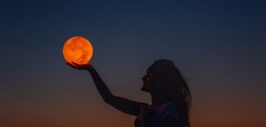 Uma mulher jovem levanta a mão como se estivesse segurando a lua cheia