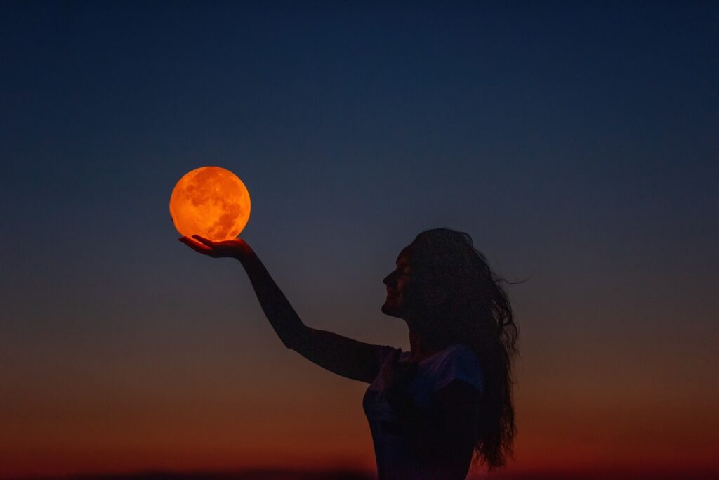 Uma mulher jovem levanta a mão como se estivesse segurando a lua cheia