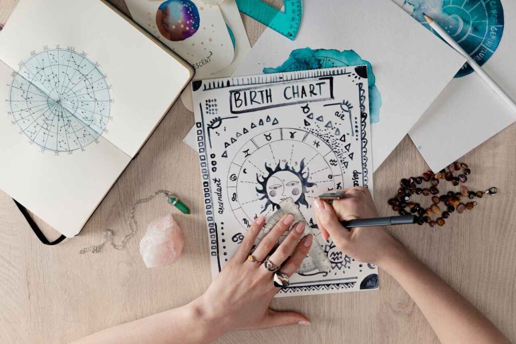 Vista superior de uma astróloga desenhando um mapa astral de nascimento com cristais e desenhos em aquarela em cartões na mesa
