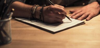 mão com lápis sob caderno de música em uma mesa de madeira