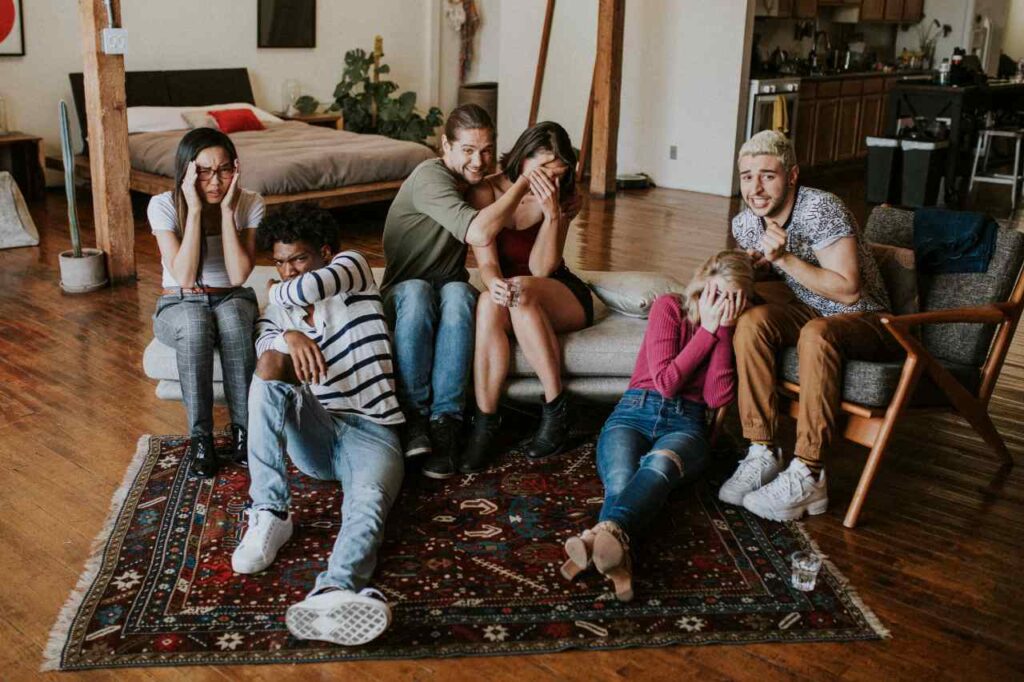 Grupo de amigos reagindo a algo na televisão, na sala de uma casa, no sofá