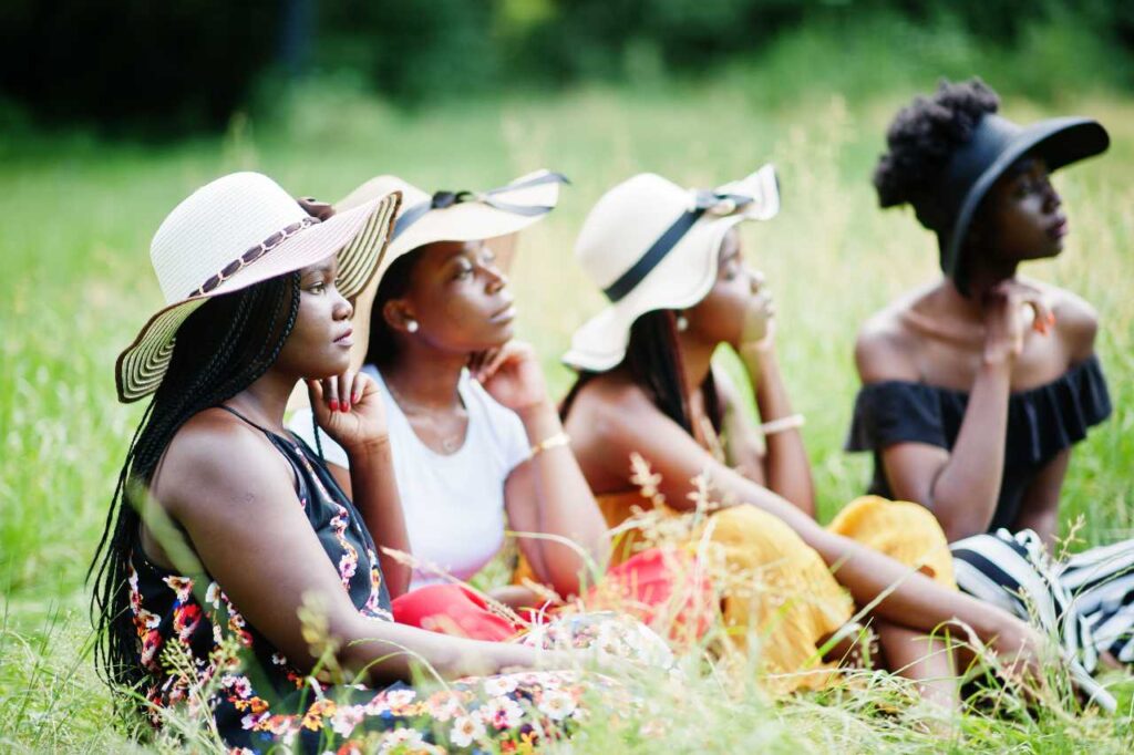 Grupo de quatro mulheres usam chapéu de verão sentadas na grama verde do parque