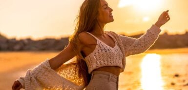 uma jovem vestindo um pequeno suéter de lã e calça de veludo cotelê na praia. Aproveitando o sol ao pôr do sol à beira-mar