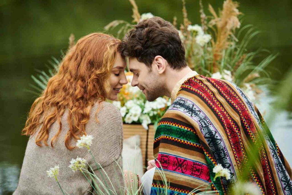 Um homem e uma mulher, vestidos com roupas de estilo boho, sentam-se juntos em um parque verdejante