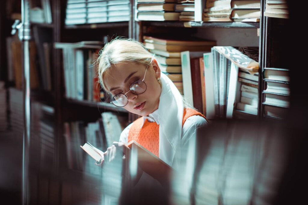 mulher de óculos lendo livro na biblioteca