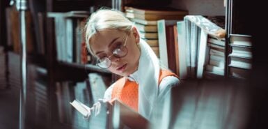 mulher de óculos lendo livro na biblioteca