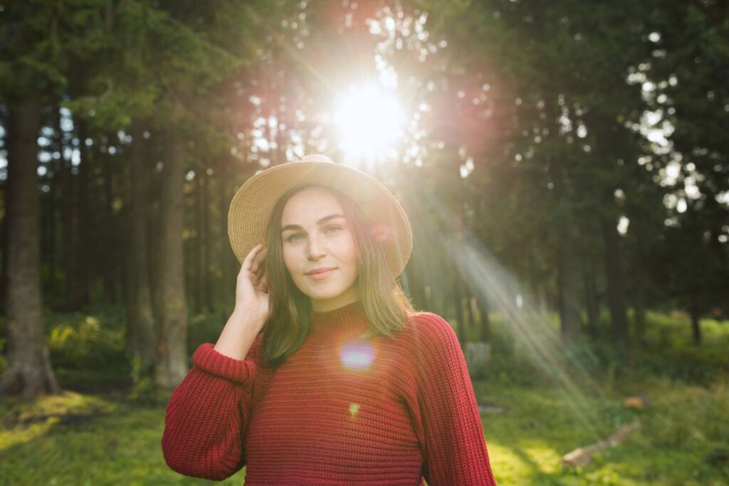 mulher com chapéu de palha em frente na contra luz do sol em um espaço de floresta