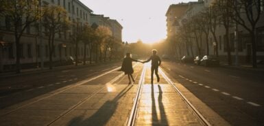 casal na contraluz do sol, entre edificações em uma linha férrea