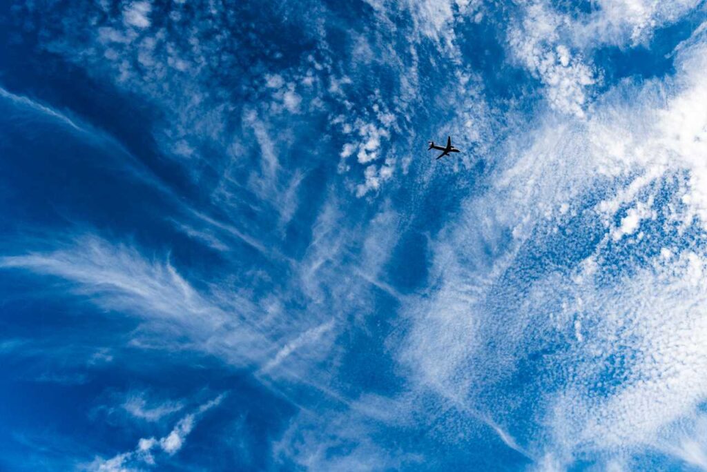 Céu azul com nuvens brancas esticadas e avião de passageiros voando alto