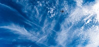 Céu azul com nuvens brancas esticadas e avião de passageiros voando alto