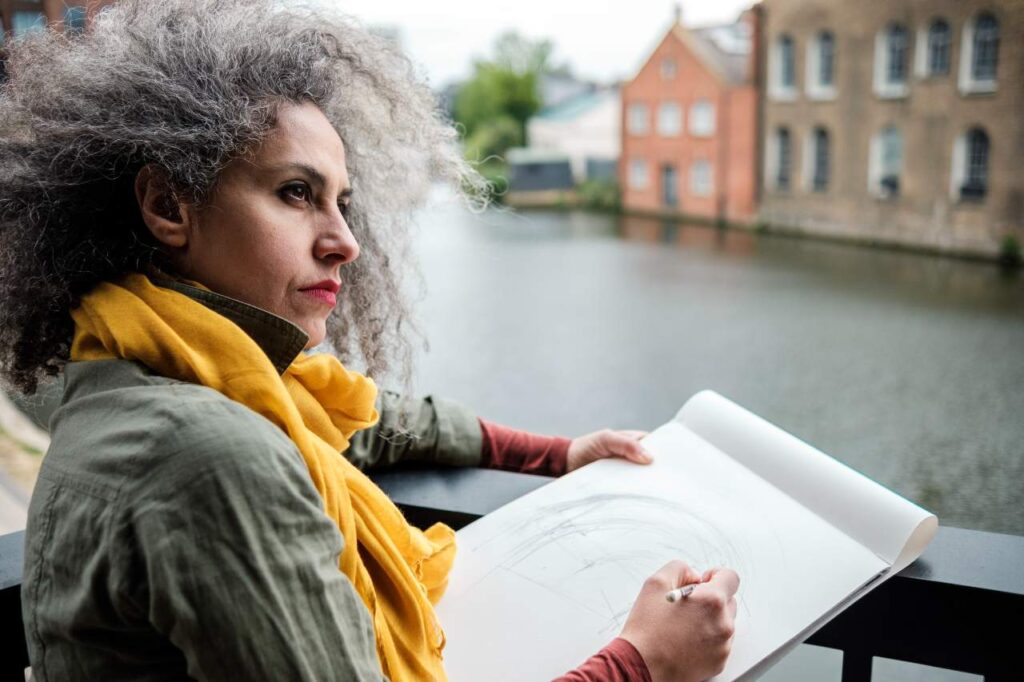 Artista mulher madura fazendo um desenho em um bloco de papel sobre um canal em Londres