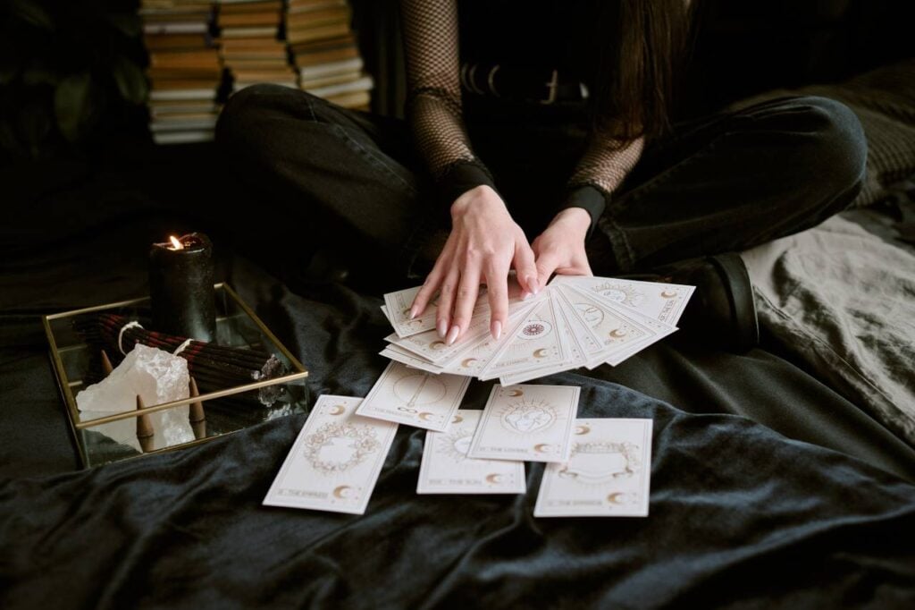 Mãos femininas tocando cartas de tarot, com vestes pretas, toalha de tarot e crista
