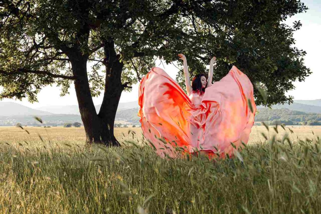 Mulher com saias esvoaçantes em um gramado com árvore frondosa ao fundo