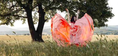 Mulher com saias esvoaçantes em um gramado com árvore frondosa ao fundo