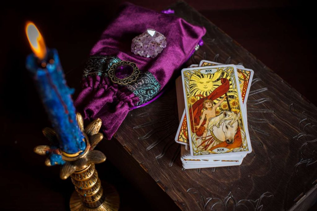 Cartomancia. Uma cartomante, cartas de tarot. Na mesa estão vela azul em um castiçal dourado, um saquinho de veludo e um cristal