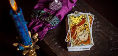 Cartomancia. Uma cartomante, cartas de tarot. Na mesa estão vela azul em um castiçal dourado, um saquinho de veludo e um cristal
