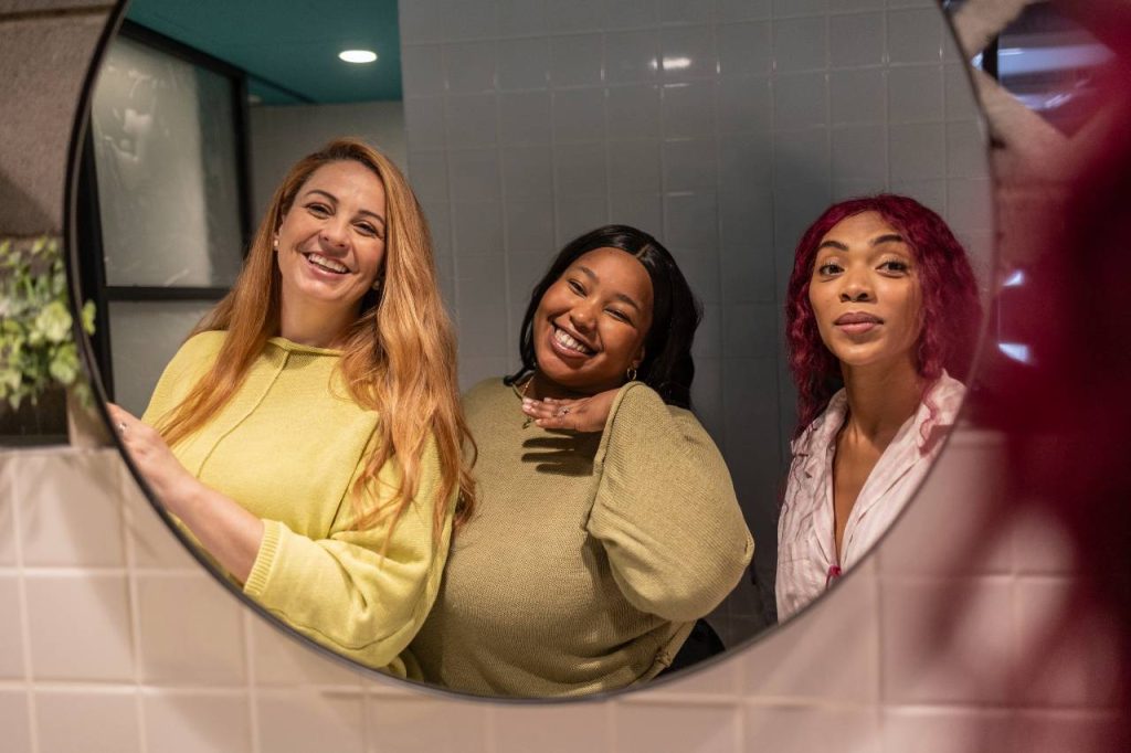 Três colegas felizes sorrindo no espelho do banheiro do escritório