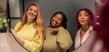 Três colegas felizes sorrindo no espelho do banheiro do escritório