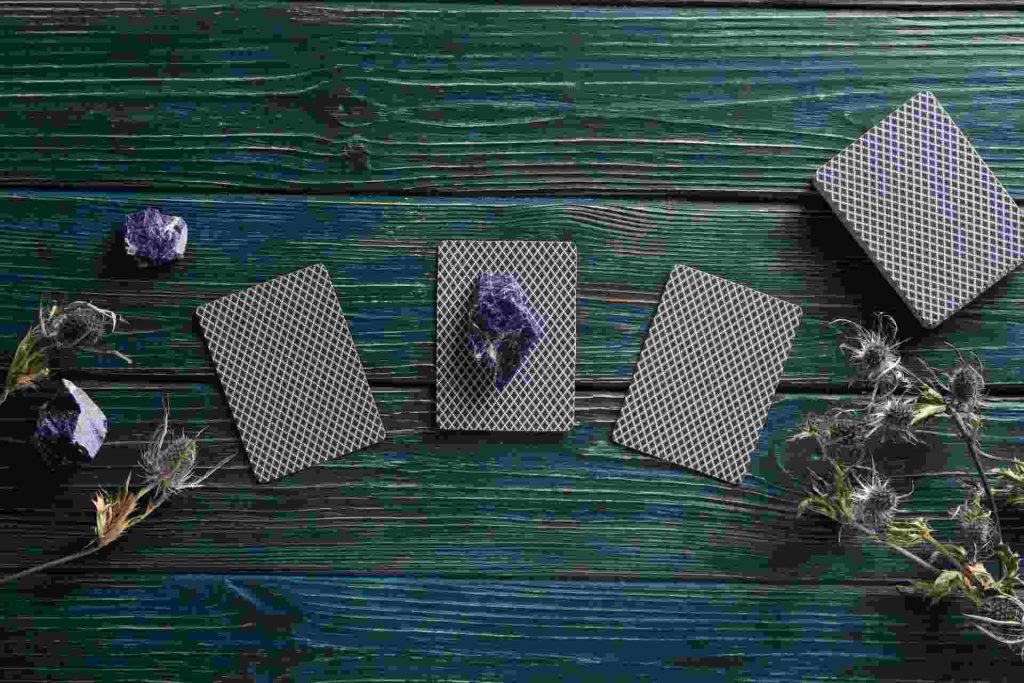 verso de cartas de tarot com alguns cristas e plantas em uma mesa de madeira pintada de azul