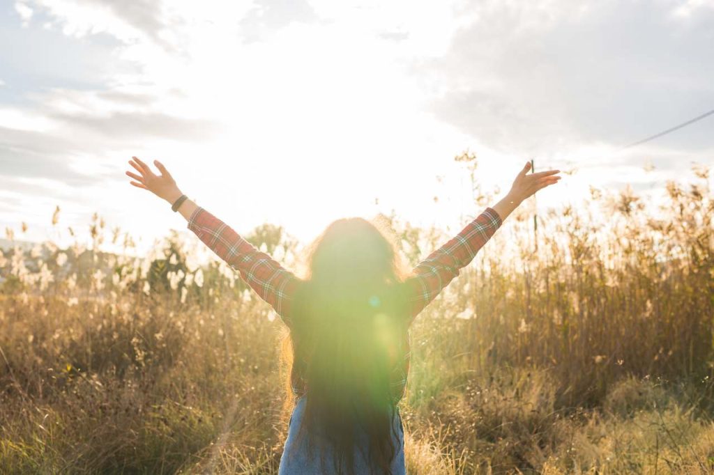 Conceito de verão, liberdade e férias - Mulher feliz levantando os braços em trigo dourado, vista traseira